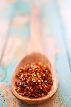 red chilli flakes in wooden spoon over wood background - selective focus