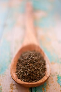 basil spice in wooden spoon over wood background - selective focus