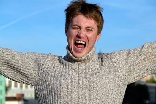 Loud shout. The young man against the blue sky.