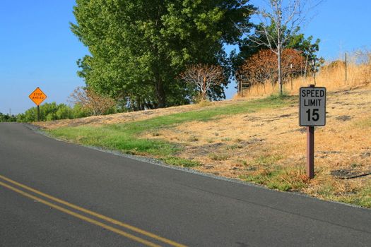 Speed limit road sign and stop ahead road sign next to a road.
