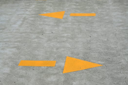 Close up of yellow arrows sign on a pavement.
