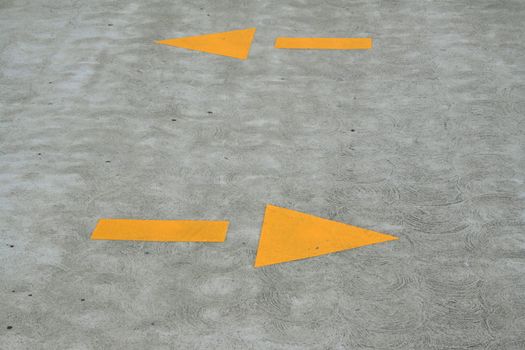 Close up of yellow arrows sign on a pavement.

