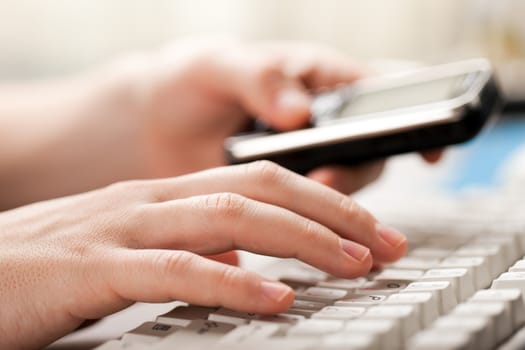 Hand holding mobile phone typing computer keyboard