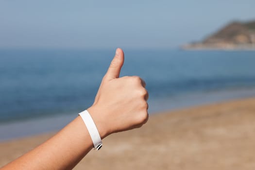 Summer vacations - woman hand gesturing thumb up success sign on sea sand beach