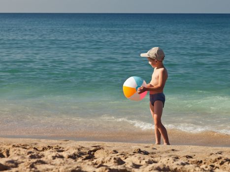 Summer vacations - little child boy hand holding inflatable ball toy on sea sand beach