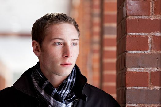 A portrait of a young man standing in an outdoor corridor during winter.