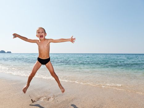 Summer vacations - little smiling child boy jumping on sea sand beach