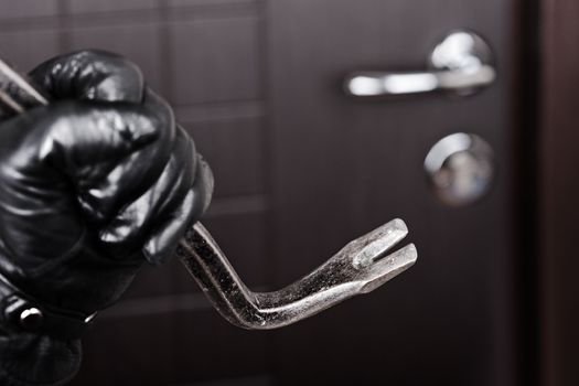 Crime scene - criminal thief or burglar hand in gloves holding metal crowbar break opening home door lock