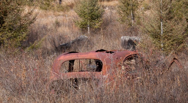 Old abandoned car in a field near a ghost town.