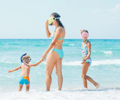 Happy young mother with her child with snorkeling equipment on sandy tropical beach