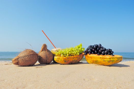 Papaya, coconut, nut and grapes on the sandy beach