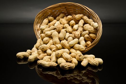 A pile of ground nut spilled from a rattan basket on a black mirror with dark grey background