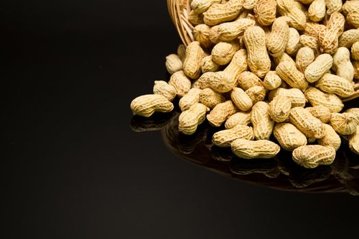 A pile of roasted groundnut spilled from a rattan basket on a black mirror with mirror image off center for copy space