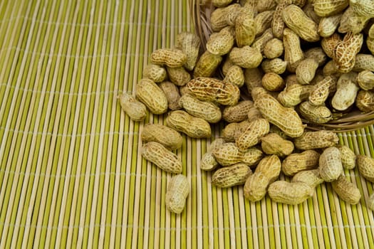 pile of groundnut spilled from a rattan basket onto a bamboo mat as background