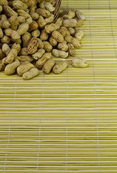 Pile of groundnut spilled from a rattan basket onto a bamboo mat in portrait orientation as background