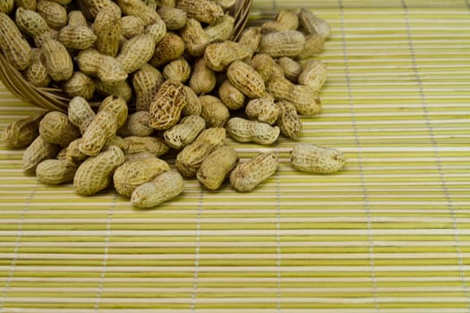 Pile of groundnut spilled from a rattan basket onto a bamboo mat in landscape orientation as background