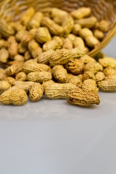 Pile of groundnut spilled from a rattan basket on a bluish grey surface in portrait orientation