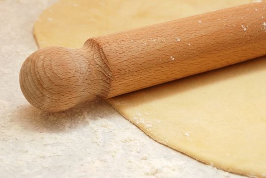 Closeup detail of a wooden rolling pin on thinly rolled out fresh pastry