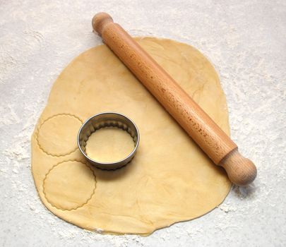Rolling pin and cutter on fresh pastry, cutting out circles on a floured surface
