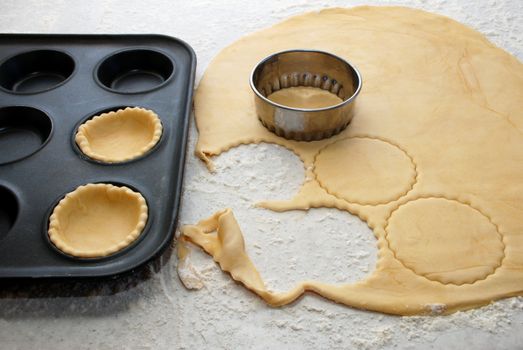 Circles being cut from fresh pastry to and filling a bun tin to make jam tarts