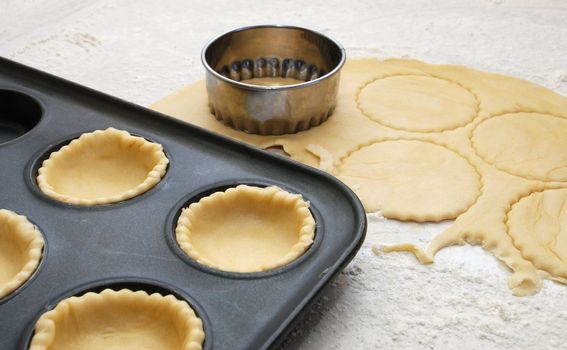 Pastry circles being cut and lining a metal bun tin for jam tarts