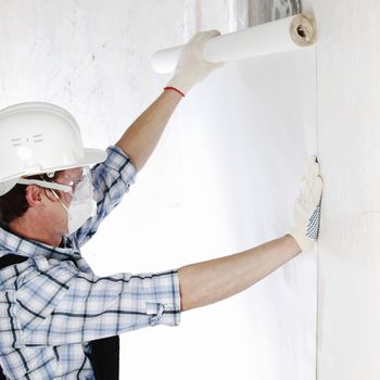 worker attaching wallpaper to wall