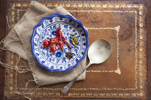 Cardamon seeds, star anise and peppers in a colorful blue bowl on a vintage table.
