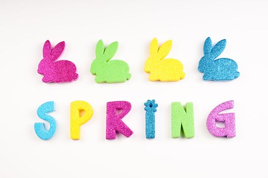 The word Spring in glitter colors of blue, yellow, purple, green.  The letters are made of foam cutouts on white background.