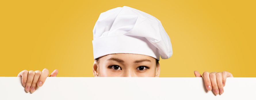 Asian female chef holding a white banner for text, hiding her face behind a poster, you can see only the eyes