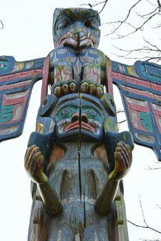 Totem pole outside on zhe background of sky and trees brunches