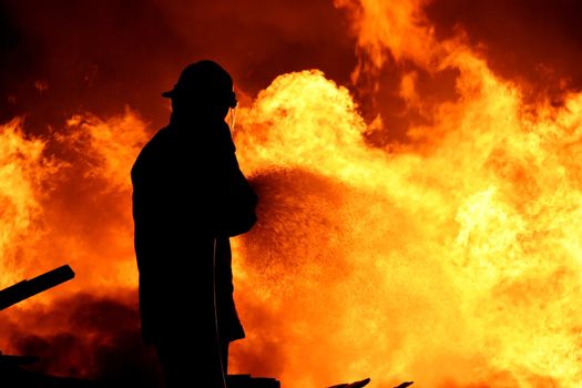 Fireman fighting a raging fire with huge flames of burning timber