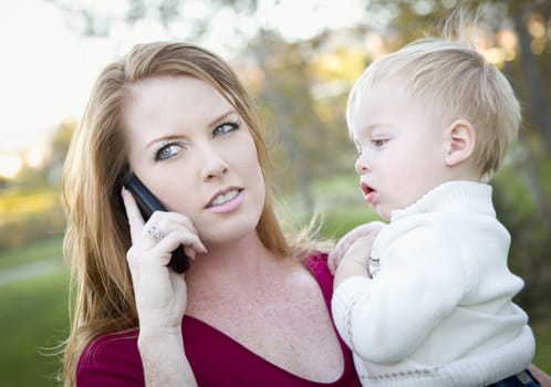Stressed Attractive Woman Using Cell Phone with Child in Arms.