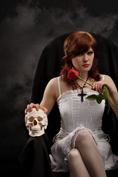 Young sexy witch sitting in a chair with a skull and rose