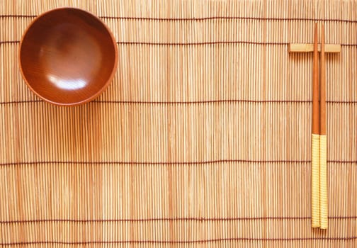 Chopsticks with wooden bowl on bamboo matting background