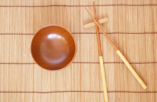 Chopsticks with wooden bowl on bamboo matting background 