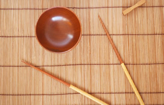 Chopsticks with wooden bowl on bamboo matting background 