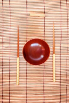 Chopsticks with wooden bowl on bamboo matting background 