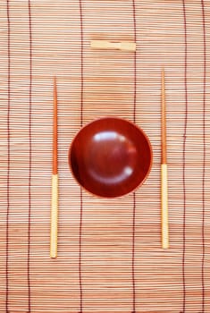 Chopsticks with wooden bowl on bamboo matting background 