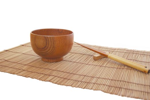 Chopsticks with wooden bowl on bamboo matting background 