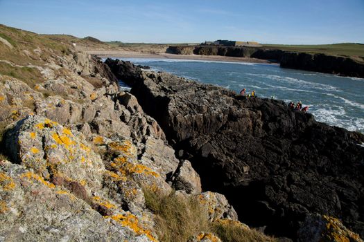 Along the Wales coast path, Cable bay, Anglesey, Wales, UK. A group on the rocks coasteering with the sea and beach in the background.