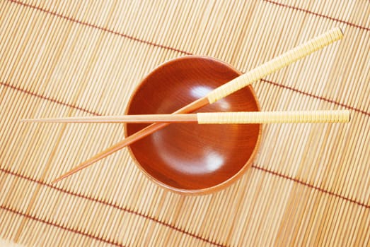 Chopsticks with wooden bowl on bamboo matting background 