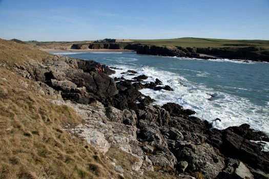 Along the Wales coast path, Cable bay, Anglesey, Wales, UK. A group on the rocks coasteering with the sea and beach in the background.