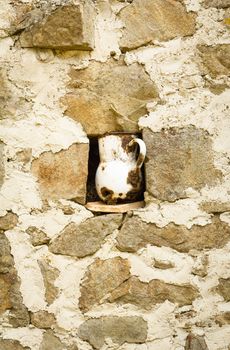 Detail of vintage metalic pitcher in a niche in stone wall