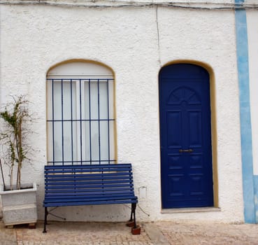 Typical whitewashed Portuguese house with blue door and blue bench outside.