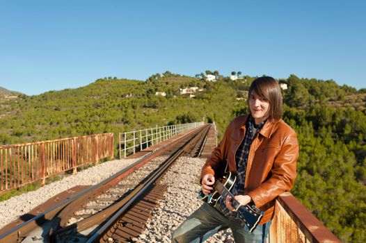 Young guitarist playing on a rusty railway bridge