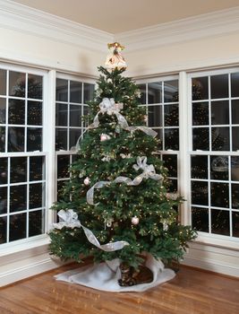 Christmas tree decorated with silver and white ribbons and ornaments in family home