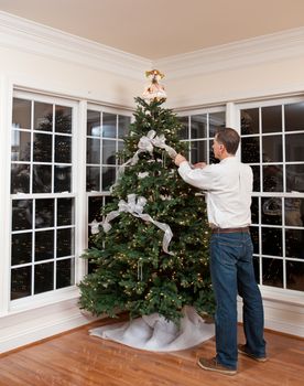 Senior man decorating a Christmas tree in family home