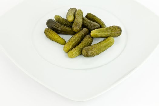 Pickled cucumbers in dish on white background.