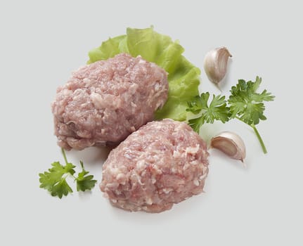 Two raw chicken rissoles with parsley and garlic cloves on the gray background