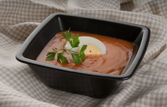Tomato soup with parsley and boiled egg in black bowl
